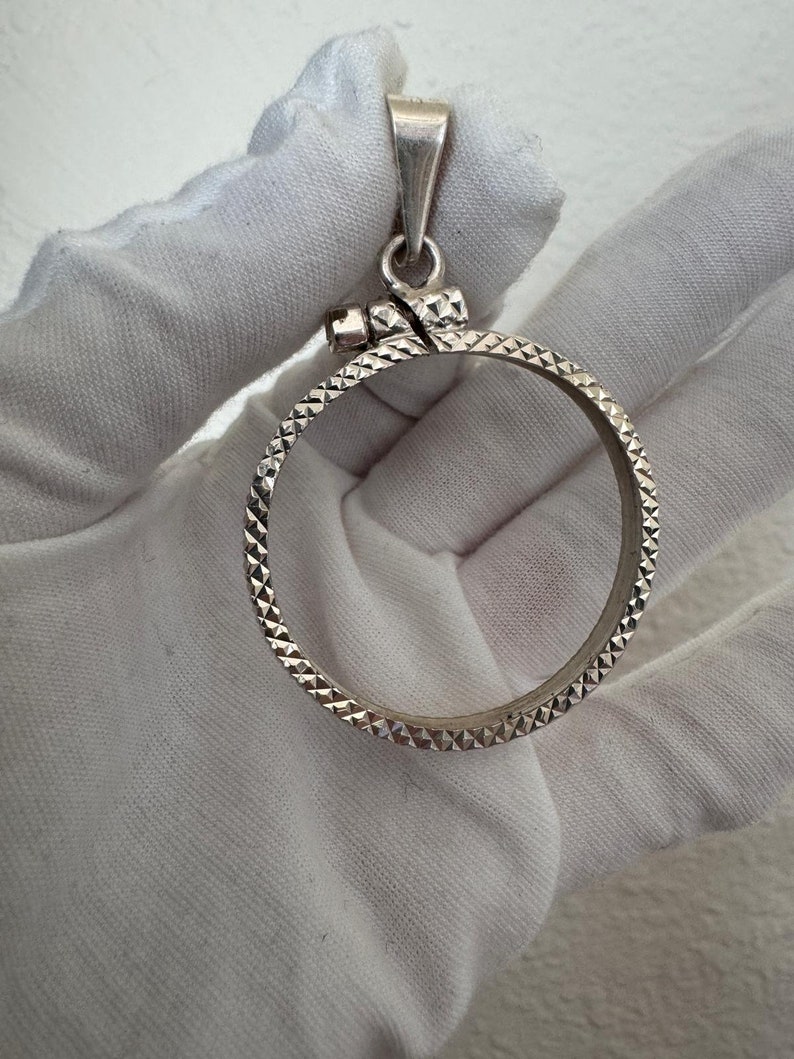 Puede incluir: Pendiente de moneda de plata con un dise&ntilde;o texturizado en forma de diamante. El pendiente tiene un bucle en la parte superior para sujetarlo a una cadena.