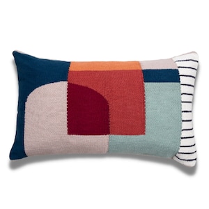 May include: A rectangular throw pillow with a geometric pattern in shades of blue, red, orange, and beige. The pillow has a white and black striped border.