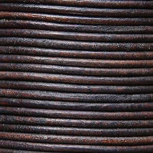 May include: Close-up of a reel of dark brown leather cord. The cord is tightly wound and has a smooth, slightly textured surface.
