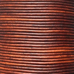 May include: Close-up of a cylindrical object made from tightly wound, dark brown leather cords. The cords have a slightly textured surface and vary in shades of brown, creating a layered effect. The overall appearance suggests a handcrafted item, possibly a decorative piece or a component of a larger product.