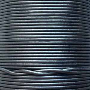May include: A close-up shot of a spool of black leather cord. The cord is tightly wound, showing a textured surface. The dark colour and cylindrical shape suggest its use in crafting or jewellery making. The cord appears to be durable and flexible.