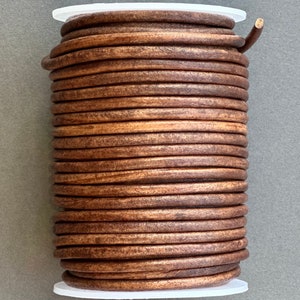 May include: A spool of brown leather cord, wound tightly in a white plastic container. The cord is smooth and has a slightly textured surface.