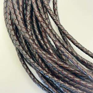 Può includere: Primo piano di diversi fili di cordoncino in pelle intrecciata marrone scuro. I cordoncini sono fittamente intrecciati, creando una superficie strutturata. Il colore è un marrone ricco e profondo con sottili variazioni di tono. I cordoncini sono probabilmente usati per la creazione di gioielli o l'artigianato.