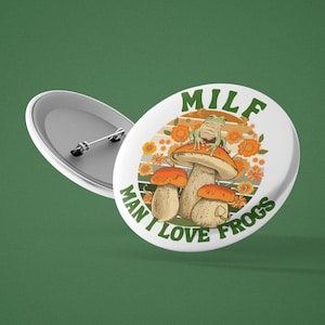 May include: White button with a green frog sitting on a mushroom with the text "MILF MAN I LOVE FROGS" in a retro style.