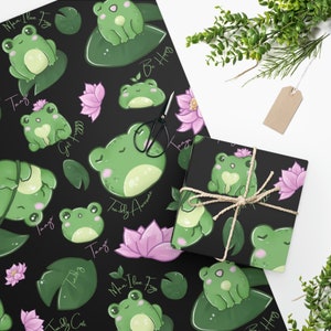 May include: Black wrapping paper with a repeating pattern of green frogs on lily pads, pink lotus flowers, and green leaves. The paper has text that says "Man I Love Frogs", "Toady Cute", "Toady Awesome", "Get Happy", "Be Happy", and "Tanya".