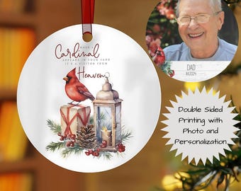 May include: A white, round Christmas ornament with a red cardinal illustration, a lantern, and text that reads "When a Cardinal appears in your yard, it's a visitor from Heaven." A second ornament shows a photo and the text "DAD 11/2024."