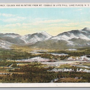 May include: A vintage postcard featuring a landscape view of mountains, including Mt. Marcy, Colden, and McIntyre from Mt. Cobble in late fall near Lake Placid, New York. The text at the top reads: MTS. MARCY, COLDEN AND MCINTYRE FROM MT. COBBLE IN LATE FALL. LAKE PLACID, N. Y. 11.