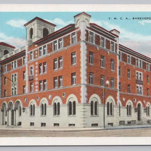 May include: A vintage postcard illustration of the Y.M.C.A. building in Shreveport, LA. The multi-story structure features red brick walls with white stone trim, arched windows on the ground floor, and two prominent towers against a blue sky.