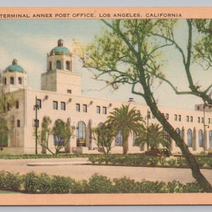 May include: Vintage postcard featuring the New Terminal Annex Post Office in Los Angeles, California. The building is a light color with a domed roof and arched windows. Palm trees and other greenery surround the building.