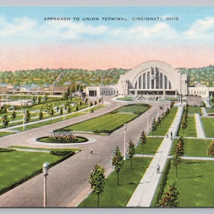 May include: Vintage postcard depicting the Approach to Union Terminal in Cincinnati, Ohio. The image shows a large building with a curved facade, surrounded by green lawns, trees, and walkways. The sky is a mix of blue and pink.