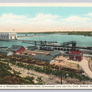 May include: A vintage postcard depicting a general view of the Mississippi River Power Plant, Government Lock and Dry Dock in Keokuk, Iowa. The postcard shows a large dam with a lock and dry dock in the foreground, and a river in the background.