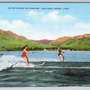 May include: Vintage postcard featuring three water skiers on Pineview Lake near Ogden, Utah. The skiers are pulled by a boat, creating white water. Lush green mountains and a blue sky form the backdrop. Text at the top reads "WATER SKIERS ON PINEVIEW LAKE NEAR OGDEN, UTAH."