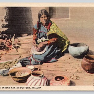 May include: A vintage postcard titled H-5511 MOKI INDIAN MAKING POTTERY, ARIZONA, depicting a person in a blue dress and yellow shawl crafting pottery. Several clay vessels, including a striped pot and a dark bowl, are arranged on the ground.