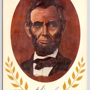 May include: A vintage postcard featuring a portrait of Abraham Lincoln in a black suit and bow tie. The portrait is set against a brown background and surrounded by a gold laurel wreath. The text "A. Lincoln" is written in cursive below the portrait, and the years "1809" and "1865" are printed at the bottom of the postcard.