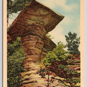 May include: A vintage postcard featuring the Visor Ledge at the Dells of the Wisconsin River. The image displays a tall, layered sandstone rock formation with a prominent overhanging ledge, surrounded by green trees under a blue sky with clouds.