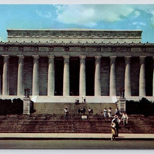 May include: A vintage postcard view of the Lincoln Memorial in Washington, D.C., featuring the large white marble structure with its prominent Doric columns, wide stone steps, and a blue sky with clouds above a group of people walking on the stairs.