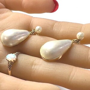 May include: A set of vintage jewelry featuring a gold ring with a white opal stone and a pair of gold earrings with pear-shaped, iridescent white pearl drops. The earrings have small pearl studs.