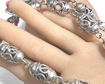 May include: A silver necklace with a series of decorative, oval-shaped beads. Each bead has an open, filigree design. The necklace is displayed against a light background.