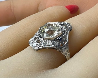 May include: A silver ring with a large, clear, octagonal-shaped gemstone surrounded by smaller diamonds and blue sapphires. The ring has a delicate, intricate design.