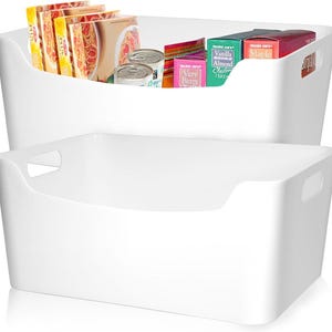May include: Two white plastic storage bins, one stacked on top of the other. The top bin contains various food items, including canned goods, cereal boxes, and pasta packages. The bins have built-in handles for easy carrying.
