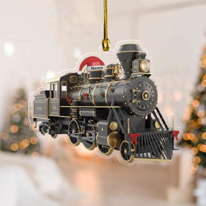 May include: A black and gold train ornament with a Santa hat that reads "202X Name". The train has gold accents, red bows, and a bell. The ornament hangs from a gold string, perfect for holiday decor.