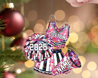 May include: A pink and white acrylic cheerleader ornament with a pom-pom, megaphone, and uniform design. The ornament has the text "CUSTOM", "NAME", and "2025". The bottom of the ornament reads "ACRYLIC - CRACKLE".