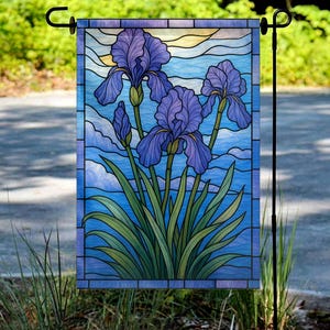 May include: A garden flag featuring a stained-glass design of purple iris flowers against a blue sky background. The flag has a rectangular shape and is displayed on a black metal stand. The iris flowers have green stems and leaves.
