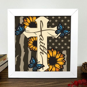 May include: A white framed print with a brown, white, and blue design. The design features a cross with the word "faith" written on it. The cross is surrounded by sunflowers and butterflies.