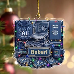 May include: A square acrylic ornament featuring a dark blue background with a laptop, keyboard, mouse, and a hoodie labeled AI ENGINEER. It includes a book titled MACHINE LEARNING, a mug with text, GPU and AI ACCELERATOR chips, and the name Robert.
