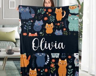 May include: A black fleece blanket with a colorful cat and floral pattern. The blanket has the name "Olivia" written in white cursive lettering.