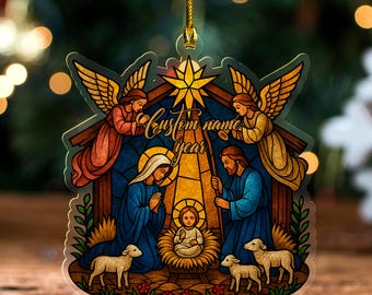 May include: A Christmas ornament featuring a stained-glass style Nativity scene. The ornament depicts Mary, Joseph, and baby Jesus, with angels and lambs. The text "Custom name year" is written across the top. The ornament is suspended by a gold string.