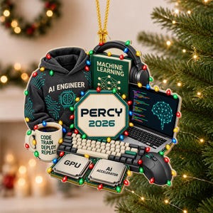May include: A decorative ornament featuring a black hoodie with AI ENGINEER text, a mug labeled CODE TRAIN DEPLOY REPEAT, a MACHINE LEARNING book, headphones, a laptop with code, a keyboard, a mouse, and chips labeled GPU and AI ACCELERATOR.