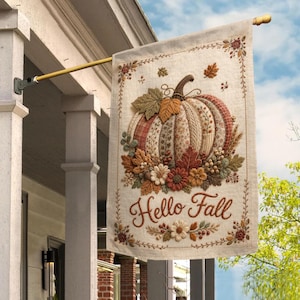 May include: A rectangular garden flag featuring a central pumpkin illustration with varied autumn-toned fabric patterns, surrounded by embroidered leaves and flowers. The text Hello Fall is written in brown script below the pumpkin.