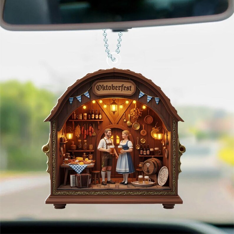 May include: A hanging car ornament shaped like a wooden tavern interior with the text Oktoberfest. The scene features two figures in traditional clothing holding beer mugs, surrounded by miniature kitchenware, a wooden barrel, and warm lighting.