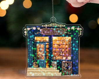 May include: A clear acrylic ornament shaped like a bookstore, with the text "Maria's Bookstore" above the entrance. The building is dark blue with a guitar and books visible. The words "ACRYLIC - TWINKLE" are at the bottom.