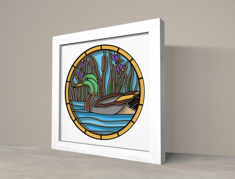May include: A framed stained glass artwork depicting a green duck swimming in blue water with yellow cattails and purple flowers.