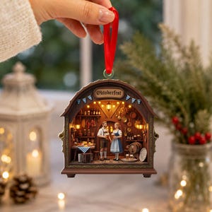 May include: A decorative hanging ornament shaped like a wooden archway with the text Oktoberfest. The interior scene depicts two figures in traditional clothing standing in a tavern with shelves, hanging kitchenware, and warm glowing lights.