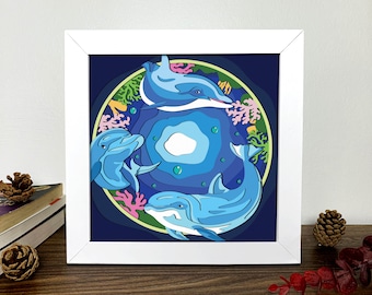 May include: A framed illustration of three blue dolphins swimming in a circle, surrounded by coral and bubbles. The background is a dark blue with a light blue center.
