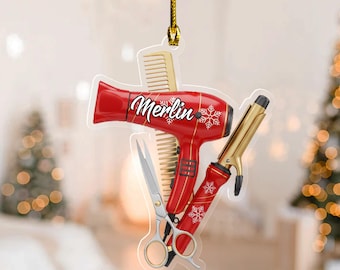 May include: A red and gold Christmas ornament shaped like a collection of salon tools. The ornament features a red hairdryer, curling iron, scissors, and comb. The hairdryer has the name "Merlin" in white script and snowflake accents.