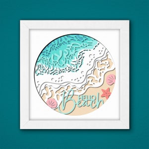 May include: A white frame with a round, paper-cut design of a beach scene. The design features blue and white waves, a sandy beach, and pink seashells. The text "Hello Beach" is written in a cursive font on the sand.