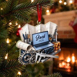 May include: A flat, hanging ornament featuring a laptop with the text 'Jack 2026' on the screen, surrounded by engineering tools including gears, a caliper, a rolled blueprint, a pencil holder, and technical drawings on a red ribbon.