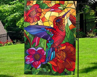 May include: A vibrant garden flag featuring a stained-glass style design. The flag showcases a red hummingbird with blue and purple wings, perched among red and pink flowers. The background has a warm, yellow and orange glow.