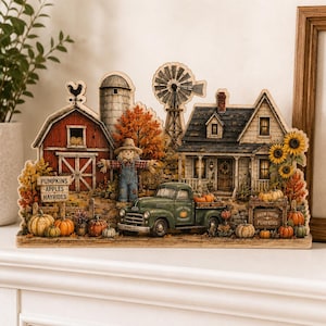 May include: A decorative wooden tabletop display featuring a red barn, a white farmhouse, a green pickup truck, a windmill, and a scarecrow. The scene includes autumn foliage, sunflowers, and pumpkins with signs reading PUMPKINS APPLES HAYRIDES and FARM FRESH PUMPKINS.