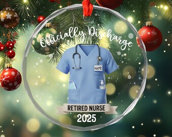 May include: A clear glass Christmas ornament with a light blue nurse's uniform design. The ornament has the words "Officially Discharged" and "Retired Nurse 2025" printed on it. A stethoscope, face mask, and hand sanitizer are also featured.