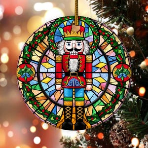 May include: Round Christmas ornament featuring a stained-glass design with a nutcracker soldier in the center. The ornament has a gold string for hanging. The nutcracker is in a red uniform with a gold crown and black boots.
