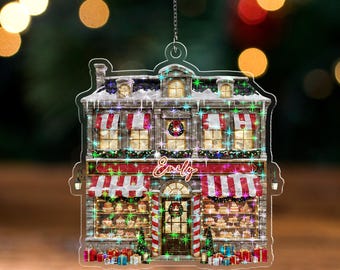 May include: A clear acrylic Christmas ornament shaped like a bakery with red and white striped awnings. The ornament has the name "Emily" on it, with a wreath on the door and Christmas presents at the bottom. The text "WAVY ACRYLIC - TWINKLE" is at the bottom.
