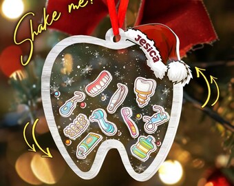 May include: A clear, tooth-shaped Christmas ornament with dental-themed illustrations inside. The ornament has a red ribbon for hanging and a Santa hat with the name "Jesica". The text "Shake me!" is written on the ornament.