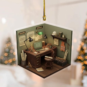 May include: A clear, hexagonal ornament featuring a miniature architectural office scene. The scene includes a desk with a laptop, blueprints, and tools. The ornament has a gold string for hanging and the text "NAME" and "20xx".