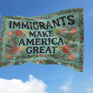 May include: A rectangular flag with the text "IMMIGRANTS MAKE AMERICA GREAT" in black letters. The flag has a teal background and is decorated with floral elements in shades of red, yellow, and green. The flag is waving in the wind against a blue sky.