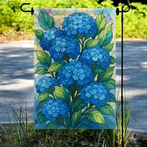 May include: A garden flag featuring a stained-glass style design of blue hydrangea flowers with green leaves. The flag is displayed on a black metal stand, adding a touch of floral elegance to outdoor spaces.